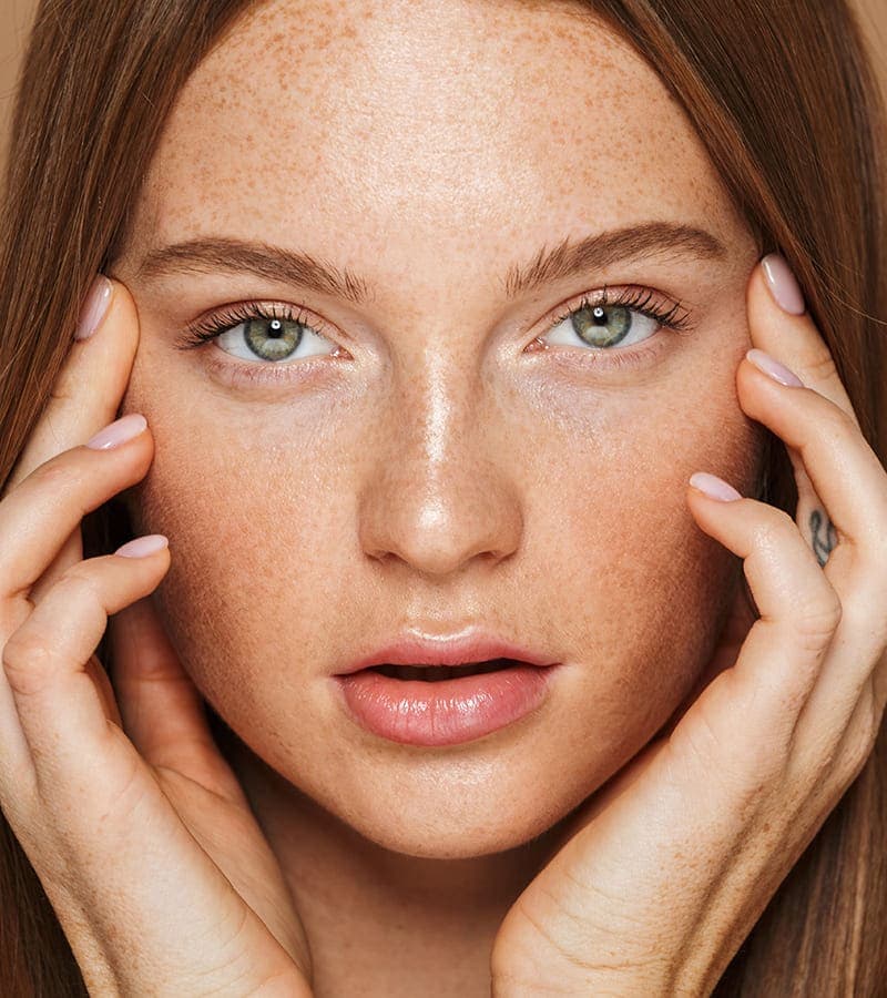 Woman with freckles touching her face peacefully
